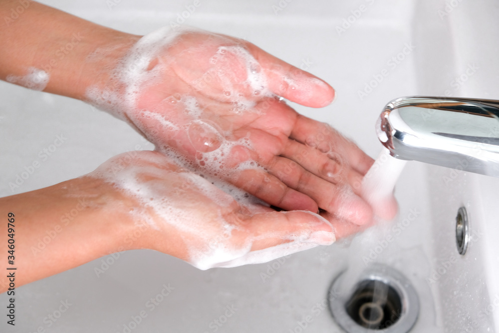 Fototapeta premium Hands of woman wash their hands in a sink with foam to wash the skin and water flows through the hands. Concept of health, cleaning and preventing germs and coronavirus from contacting hands