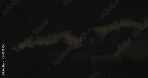 Dramatic night shot of white smoke eminating from a factory chimney with red lights shining through the smog photo