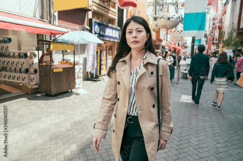 Happy young asian woman smiling outdoors and walking on city street at sunny time wearing spring clothes. confident female office worker relax going home after work passing through teeming area.