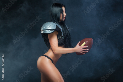 American football. Young sporty brunette wearing sexy uniform of rugby football player posing with ball in smoke isolated on black background photo