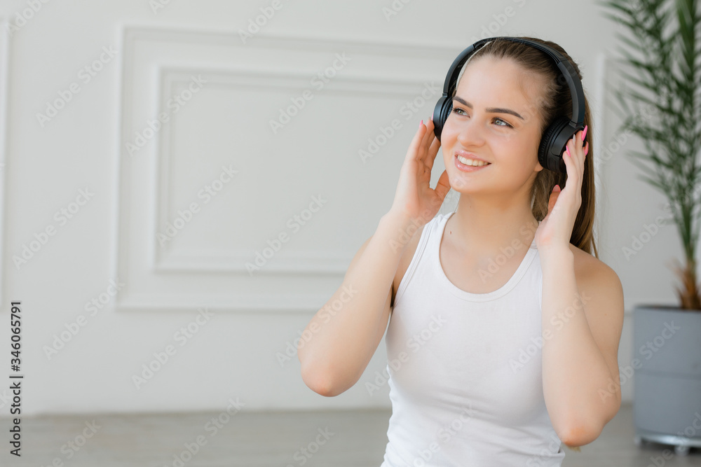 Girl in white tank top smiling and enjoying the energetic music of black headphones on white background Girl in white tank top smiling and enjoying the energetic music of black headphones on white background