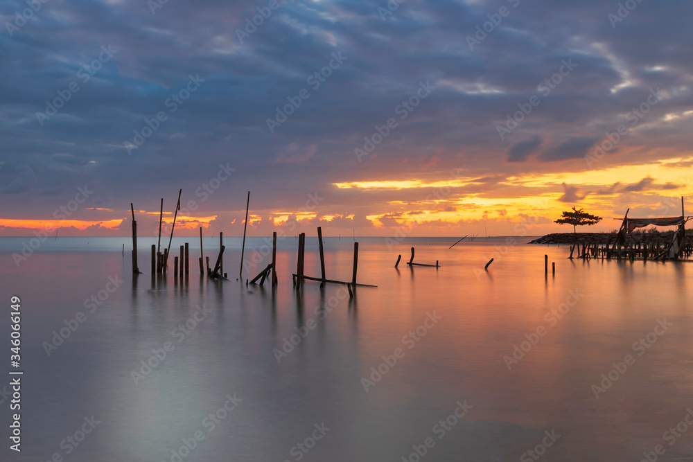 Morning scenery with rain clouds in the sky and golden light from the sun at a fishing village with an old, broken wooden bridge.
