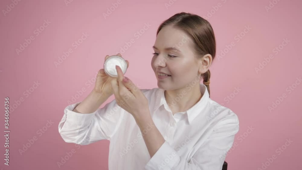 Natural thick face cream in a glass jar. The girl holds a cream in her hands and tries it with her hand.