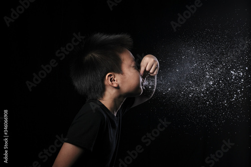 Kid of sneezing, coughing, shocking food concept. A little Asian boy of 8 years old covered nose while sneezing and Causing the water to flow out of the mouth with black background. photo