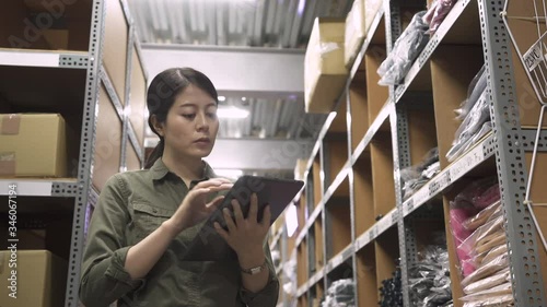 elegant asian woman manager holding digital tabelt in warehouse. wholesale logistic people and export concept. female business owner using touch pad computer in distribution stockroom indoors. photo