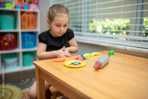 Close up of child playing with play dough in a playroom on a wood table. Girl molding modeling clay. Child playing and creating from play dough.