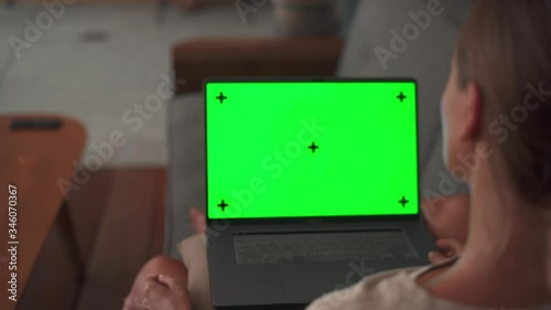 Woman watching on laptop green screen sitting reaxed on sofa photo