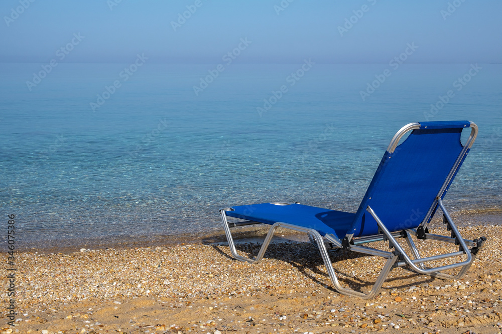 Blue lonely deck chair on the sea beach. Sunny day, Halkidiki, Greece. Blue lonely deck chair on the sea beach. Sunny day, Halkidiki, Greece.