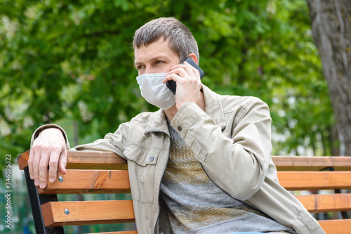 A man sits on a bench in a medical mask and talks on the phone