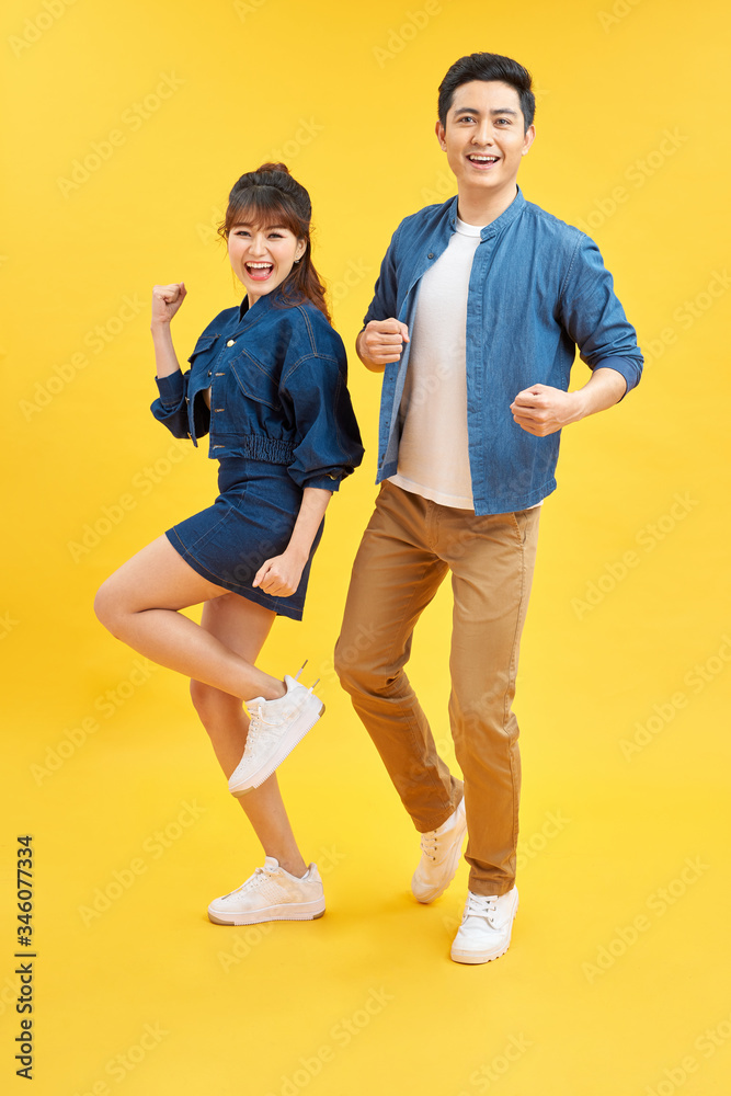 Portrait of funky couple jumping in air holding hands up enjoying time together isolated on yellow background Portrait of funky couple jumping in air holding hands up enjoying time together isolated on yellow background