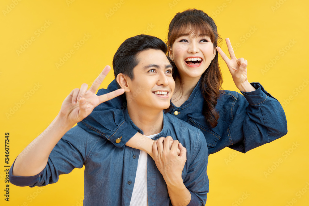 Happy cheerful man carrying his girlfriend on the back and showing two fingers Happy cheerful man carrying his girlfriend on the back and showing two fingers