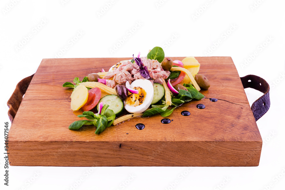 Salad with tuna, fresh vegetables - cucumber and tomatoes, canned corn, boiled potatoes, herbs, onions, olives on a wooden tray, board, dish. The object is isolated on a white background. Salad with tuna, fresh vegetables - cucumber and tomatoes, canned corn, boiled potatoes, herbs, onions, olives on a wooden tray, board, dish. The object is isolated on a white background.