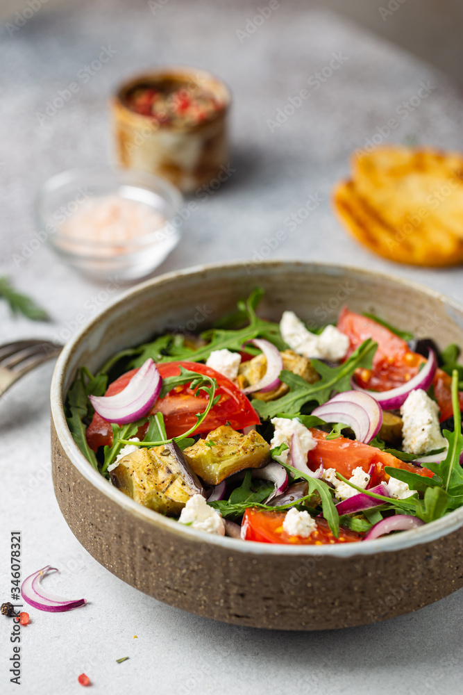 Eggplant salad with tomatoes, arugula and feta cheese in a bowl on white background