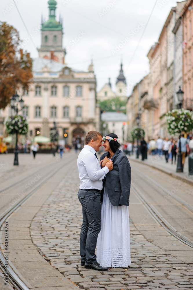 Fototapeta premium Wedding photo session In the center of the old city. The groom gave his bride his jacket so that she would warm herself. The couple hugs and smiles at each other. Rustic style wedding photography