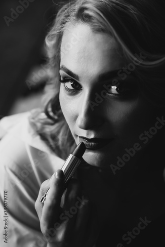 Portrait of a beautiful woman with lipstick in her hands in low key. Black and white art photo. Soft selective focus.