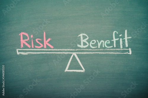 Text word risk and benefit balance on seesaw drawing writing on chalkboard or blackboard background. Concept of risk and benefit analysis in business, financial and investment. Real photo.
