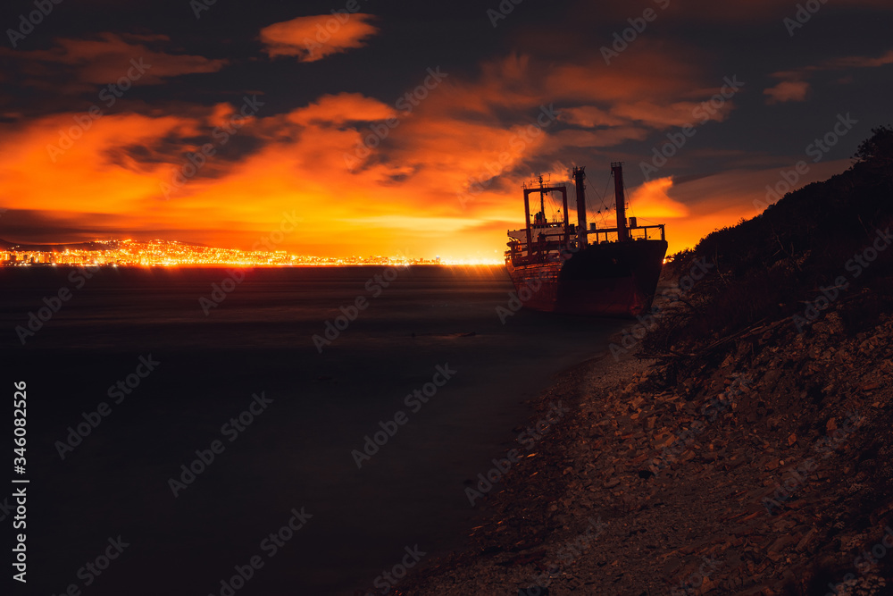 Abandoned broken ship ran aground on shore after storm. Ship graveyard. Big dry-cargo ship at night.
