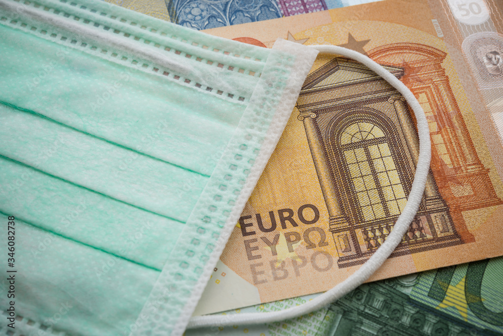 Obraz premium Face mask on Euro banknotes bill background. Global novel coronavirus (Covid-19) outbreak effect to EU, world economy, financial crisis, investment, stock market. Coronavirus pandemic in Europe.