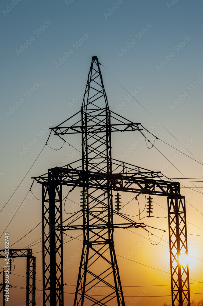 Electric post with wires with sunset background. Transmission tower. Power lines on a colorful sunset. Close up high voltage power lines silhouette. High voltage electric transmission pylon tower.