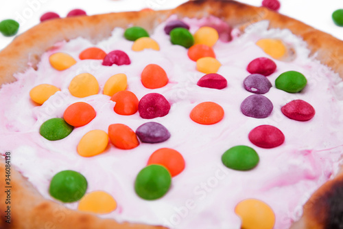 Sweet pizza with marshmallow sauce and colored sweets on a white background