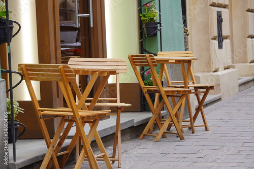 A place for outdoor summer terraces and cafes, to drink coffee on city street. Empty wooden tables and chairs, prohibition of coronavirus, reopening after lockdown. Urban romance outdoor. Tourism © Alexkarankevich