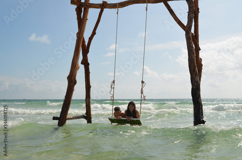 Happy mother and son having fun on a swing in the sea in summer vacation