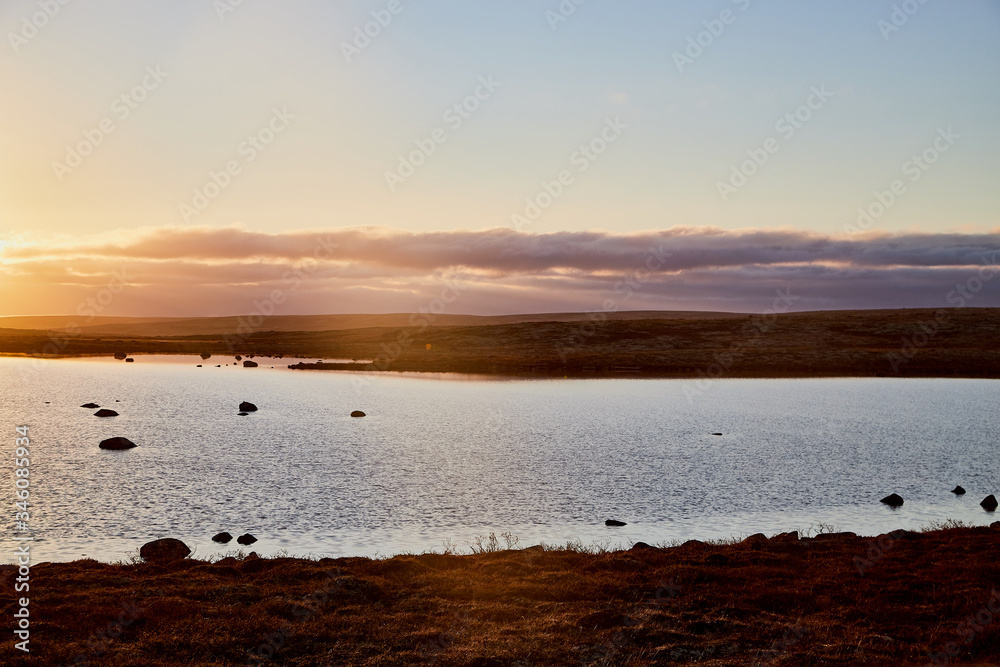 Beautiful landscape with lake, yellow sunset or sunrise over water and tundra in summer, spring or autumn evening or morning. The rays of the sun over the tundra, river on the background of blue sky