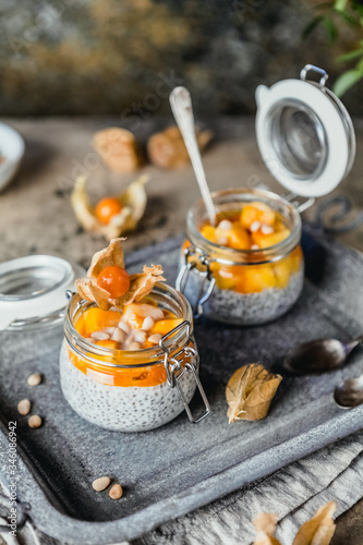  pudding with chia seeds in jars with mango slices and pine nuts on shabby beige background, healthy breakfast concept