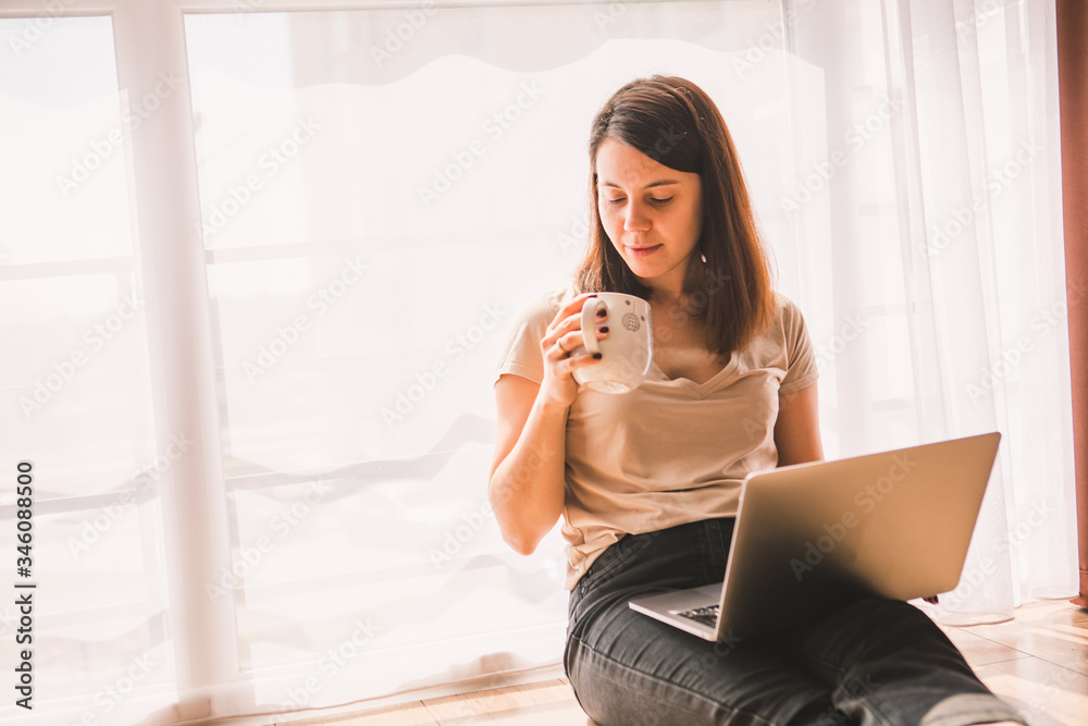 woman sitting on the floor working on laptop near big window woman sitting on the floor working on laptop near big window