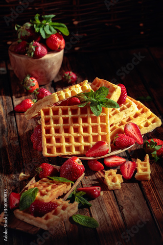 Waffles with strawberries and mint on a wooden table.