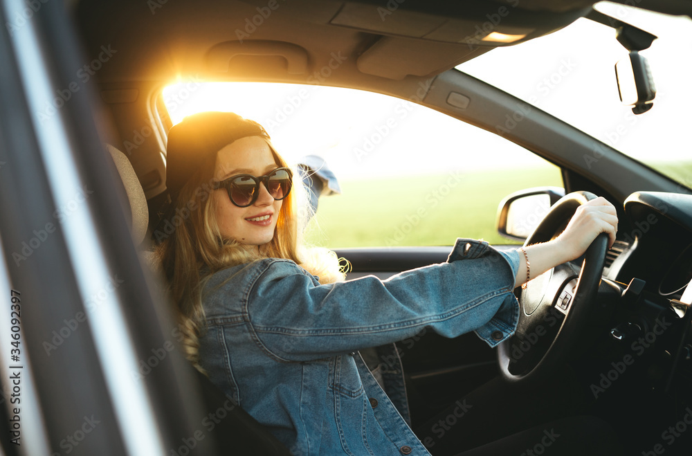 Naklejka premium Young beautiful blonde girl are smiling and having fun while driving the car. Adventure, travel, trip, tourism, driving car concept.