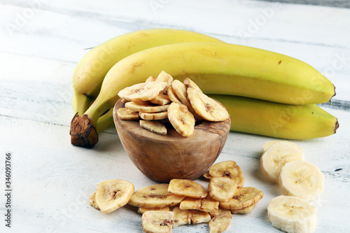 Homemade Dehydrated Banana Chips in a Bowl and fresh banana and slices on background