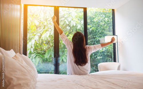 Rear view image of a woman do stretching after waking up in the morning , looking at a beautiful nature view outside bedroom window