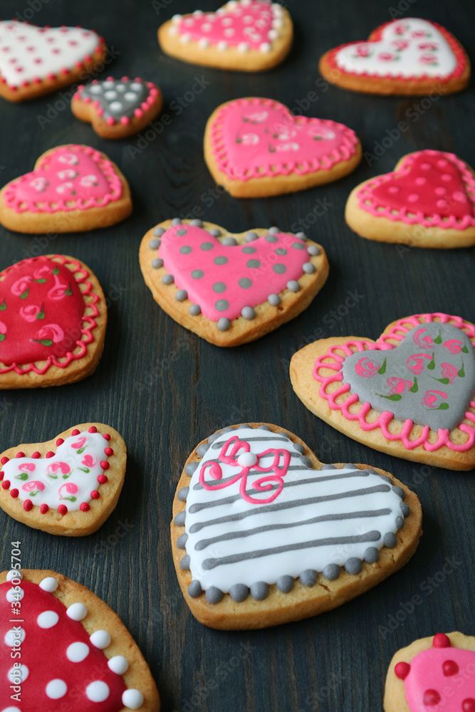 Vertical image of patterned heart shaped royal icing cookies scattered on dark brown wooden background Vertical image of patterned heart shaped royal icing cookies scattered on dark brown wooden background