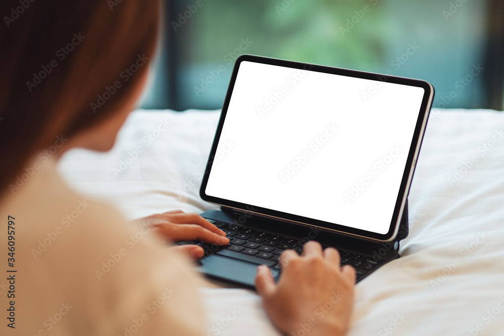 Mockup image of a woman using and typing on tablet pc with blank white desktop screen as computer pc while lying down on a cozy white bed at home Mockup image of a woman using and typing on tablet pc with blank white desktop screen as computer pc while lying down on a cozy white bed at home