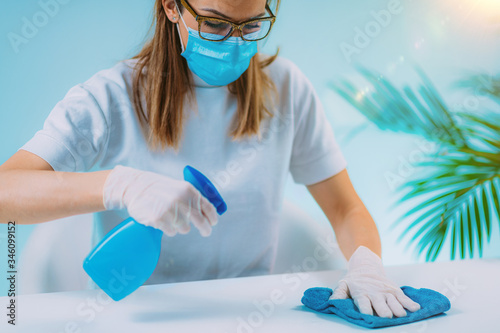 Obraz na płótnie Disinfect - Woman Spraying Table Surface with Disinfectant and Wiping it with a