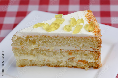 A piece of lemon sponge cake with cream served on a white plate over red plaid tablecloth. Italian concept.
