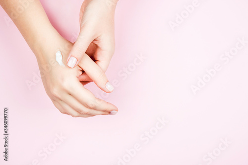 Delicate female manicure on a pink background. Well-groomed female hand with cream on the skin.