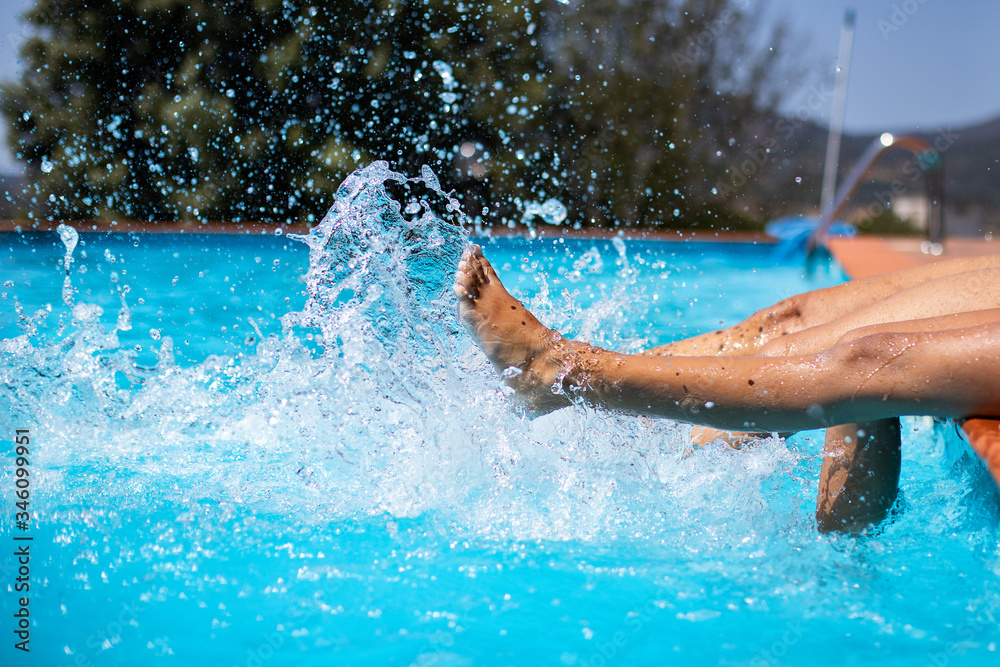 Two people splashing water with their legs at the swimming pool