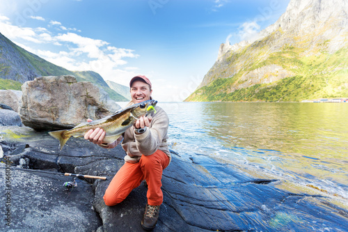 Happy man with a fish in his hands. Fishing in Norway in the fjord. Mountains on the background.