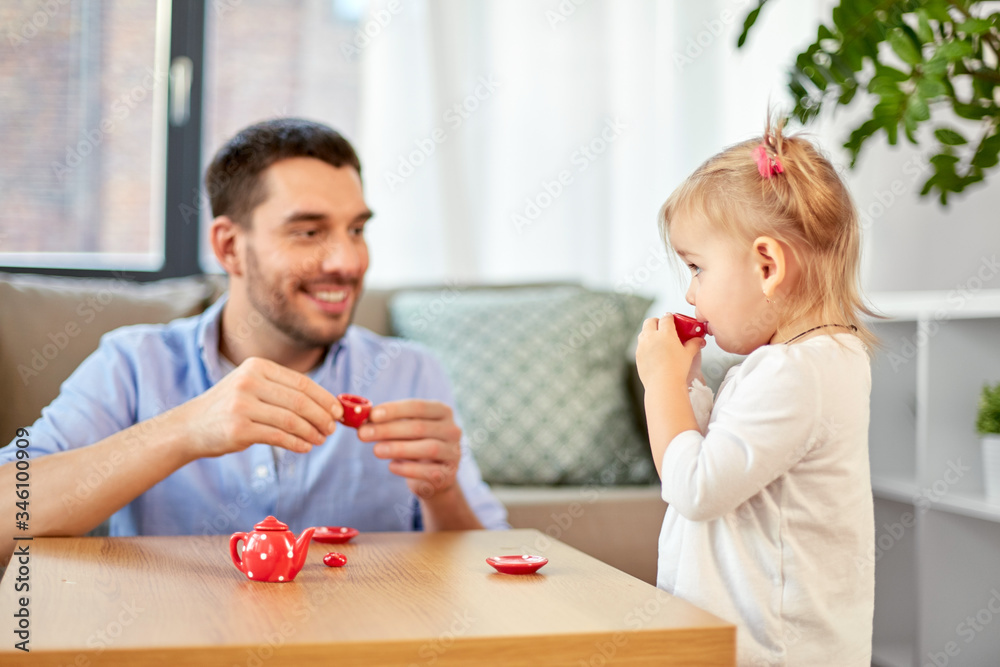 family, fatherhood and childhood concept - happy father and little daughter with toy crockery playing tea party at home