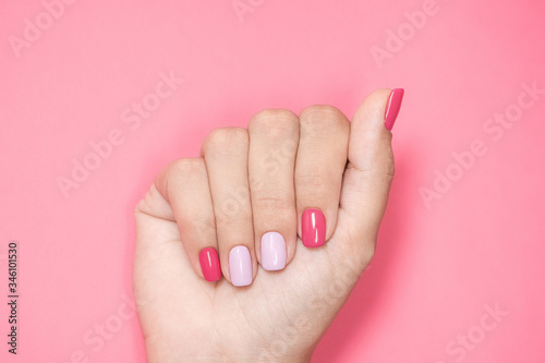 Closeup top view flatlay photography of one beautiful manicured female hand isolated on pink background. Woman with trendy colorful two colours modern nail design of bright pink and purple colors.