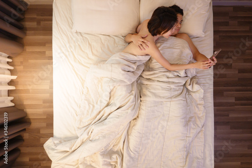 Couple using smartphone lying on bed together, boyfriend and girlfriend online social networks .