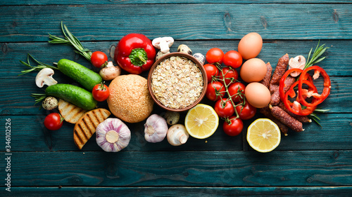 Ingredients for breakfast: Eggs, oatmeal, sausages and fresh vegetables on a blue wooden background. Top view. Free space for your text.