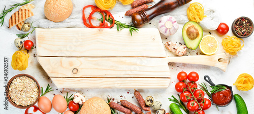 White wooden food background: tomatoes, pasta, spices, vegetables and sausages. Top view.