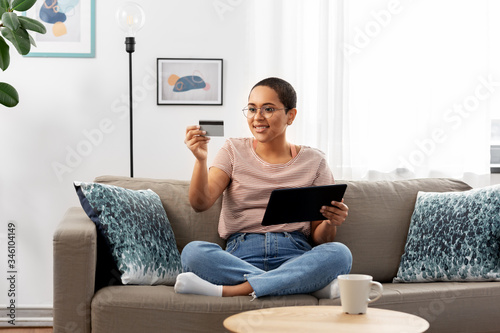 internet banking, online shopping and technology concept - happy smiling african american woman sitting on sofa with tablet pc computer and credit card at home