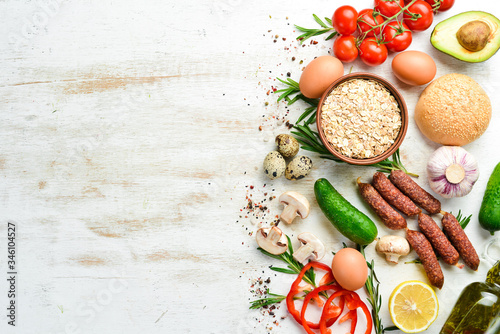 Ingredients of healthy nutrition. Cooking background: Eggs, oatmeal, sausages and fresh vegetables on a white wooden background.