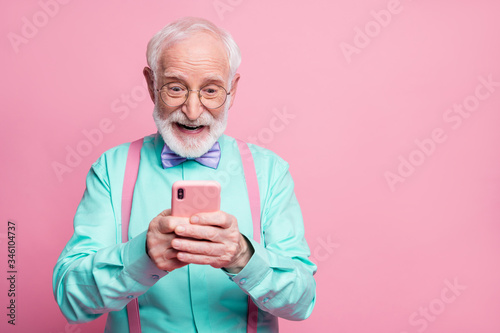 Portrait of surprised crazy shocked old man use smartphone read social media news enjoy comments wear teal outfit purple violet bow tie isolated pastel pink color background photo