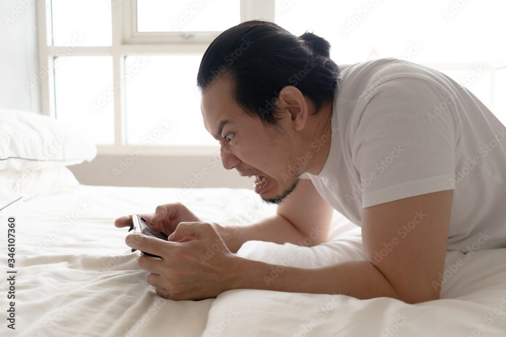 Angry and furious Asian man is addicted to mobile game. Angry and furious Asian man is addicted to mobile game.