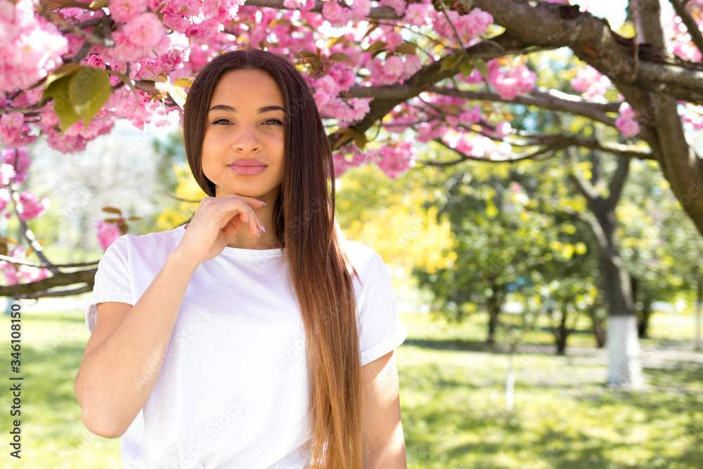 Young brunette girl in the park admires the trees of cherry blossoms